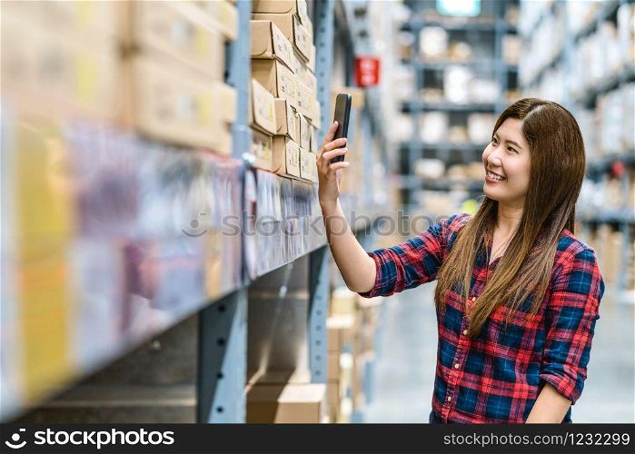 Asian woman scanning the QR code via smart mobile phone for checking goods stock and price in warehouse, customer shopping and self service, business furniture and storehouse industry concept