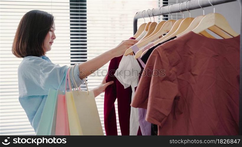Asian woman shopping clothes. Shopper looking at clothing on the rail indoors in clothing store. Beautiful happy smiling asian woman model. Medium shot.