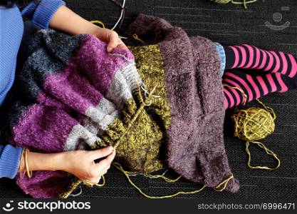 Asian woman sit on floor of home to knit woolen blanket for warm in wintertime, knitting is hobby in leisure activity to make handmade gift, photo of woman hand working from top view on day