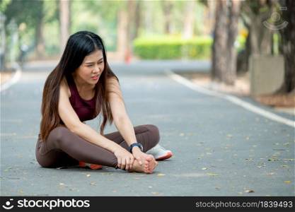 Asian woman sit on road floor and hold her foot look like she got pain and injury during exercise in park or garden in the morning.