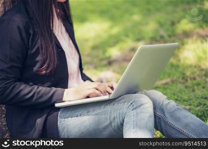 Asian woman sitting green park using laptop computer. Woman working on laptop happy entrepreneur business using notebook with hands typing on keyboard home office during coronavirus quarantine period