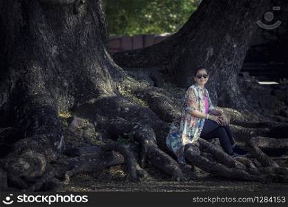 asian woman sitting on big rain tree root in traveling destination