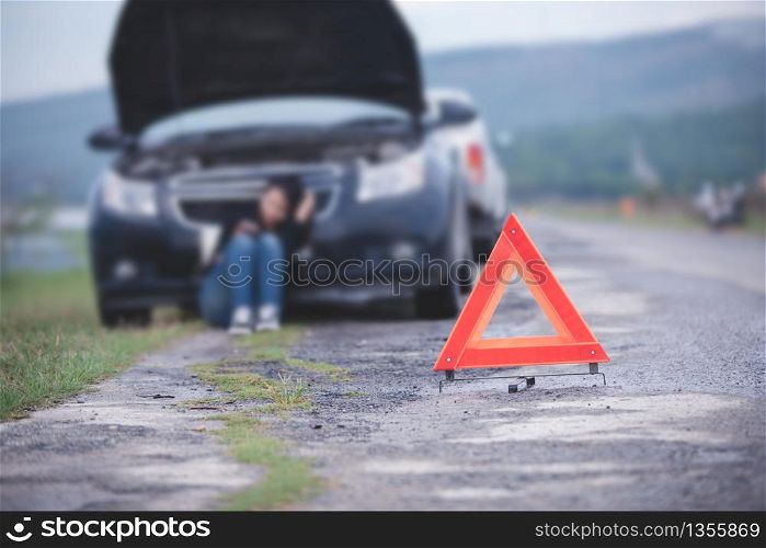Asian woman sitting on floor near broken down car with Red triangle of a car on the road