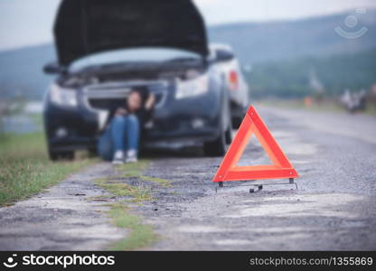 Asian woman sitting on floor near broken down car with Red triangle of a car on the road
