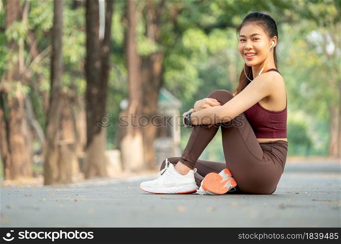 Asian woman smile and sit with one&rsquo;s knees up on road of park or garden also look at camera.