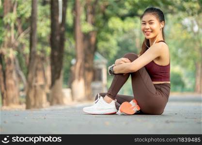 Asian woman smile and sit with one&rsquo;s knees up on road of park or garden also look at camera.