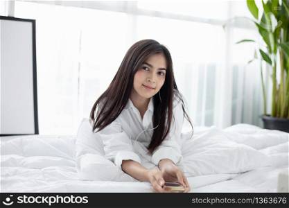 Asian woman Smile feel carefree and she lying on the bed in the morning and young beautiful girl will listening to music on headphones