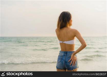 Asian woman smiling on sand beach. Young happy female in bikini relax and fun smile near tropical sea when sunset while holiday, vacation, summer trip concept.