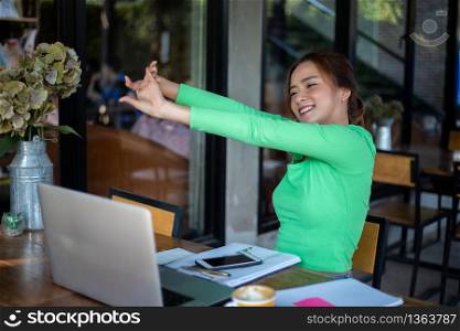 Asian woman stretching after reading book and work hard and smiling in coffee shop
