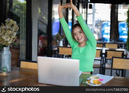 Asian woman stretching after reading book and work hard and smiling in coffee shop