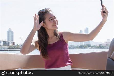 Asian woman taking selfie while sitting on boat with background of beautiful landscape. Travel and Lifestyle Concept.