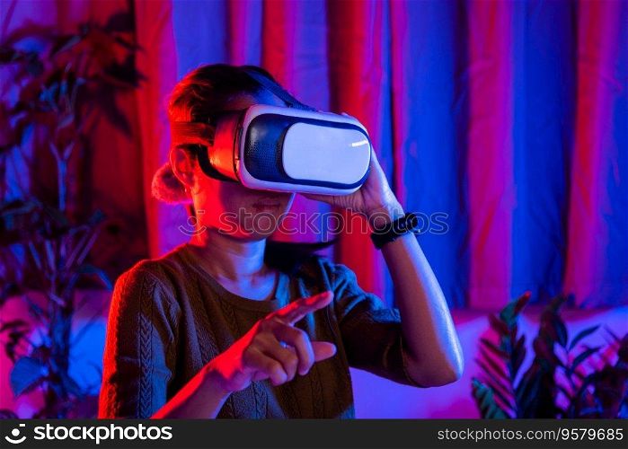 Asian woman touching air during the VR experience at home purple and blue background, female experiencing virtual reality goggles experiencing reality, metaverse and cyberspace concept