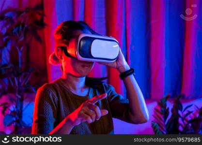 Asian woman touching air during the VR experience at home purple and blue background, female experiencing virtual reality goggles experiencing reality, metaverse and cyberspace concept