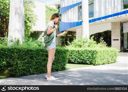 Asian woman tourist backpacker smiling and using smartphone traveling alone holidays outdoors on city street in Bangkok - Thailand.