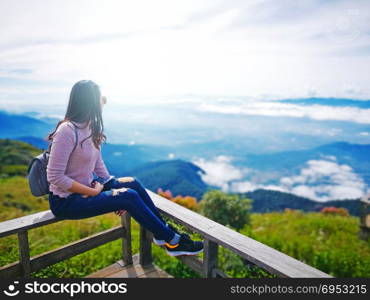 Asian woman trekker sitting on wooden terrace admiring beautiful mountain scenery