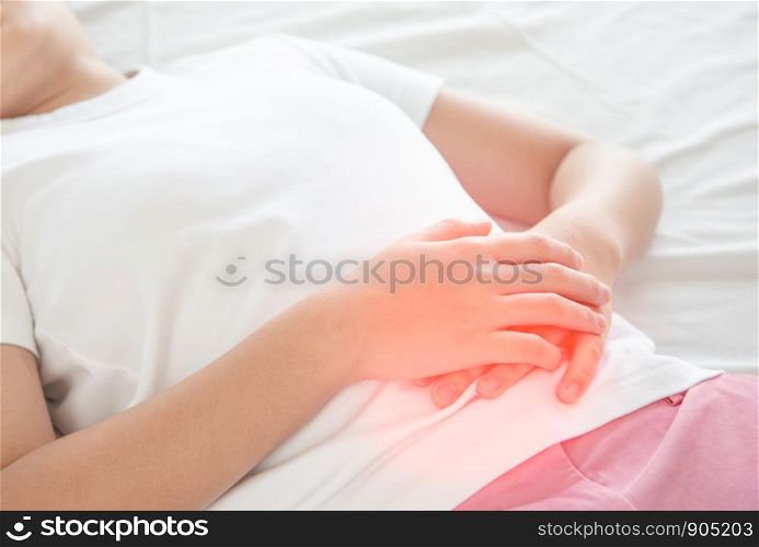 Asian woman unhappy lying on the bed looking sick, suffers from stomach ache in the bedroom, stomachache because of menstruation and eating spoiled food, Chronic gastritis. Abdomen bloating concept