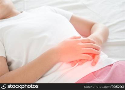 Asian woman unhappy lying on the bed looking sick, suffers from stomach ache in the bedroom, stomachache because of menstruation and eating spoiled food, Chronic gastritis. Abdomen bloating concept