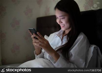 Asian woman using a mobile phone on night at the bed.She smiles and enjoys at home.