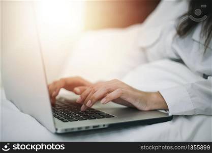 Asian woman using a notebook to work on the bed.She smiles and enjoys working at home.