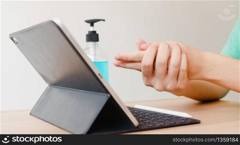 Asian woman using alcohol gel sanitizer wash hand before using tablet for protect coronavirus. Female push alcohol to clean for hygiene when social distancing stay at home and self quarantine time.