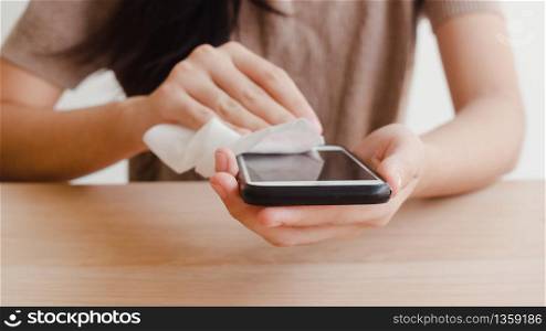 Asian woman using alcohol spray on tissue clean mobile phone before use it for protect coronavirus. Female clean surface for hygiene when social distancing stay at home and self quarantine time.