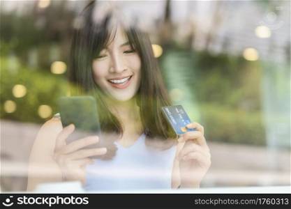 Asian woman using credit card with mobile phone for online shopping in modern coffee shop, technology money wallet and online payment concept, credit card mockup
