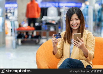 Asian woman using credit card with mobile phone for online shopping in department store over the clothes shop store background, technology money wallet and online payment concept, credit card mockup