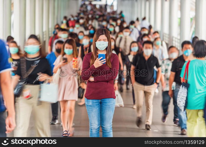 Asian woman using mobile phone between Crowd of blurred unrecognizable business people wearing surgical mask for prevent coronavirus Outbreak in rush hour working day at Bangkok transportation