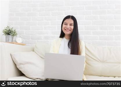 Asian woman using notebook on sofa in white room