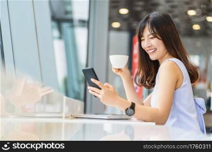 Asian woman using smart mobile phone for online shopping in modern coffee shop, holding and drinking coffee, technology money wallet and online payment concept, credit card mockup