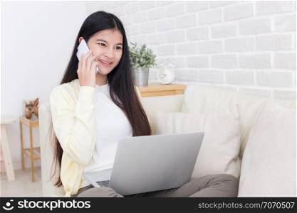 Asian woman using smartphone and laptop on sofa in white room