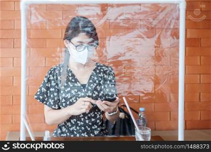 Asian woman using smartphone during dining time in restaurant with separated of shield plastic partition, protect coronavirus inflection. social distancing, new normal and life after covid-19 pandemic
