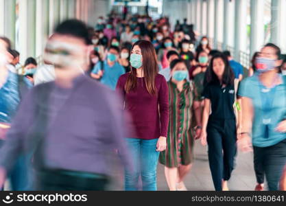 Asian woman walking and standing between Crowd of blurred unrecognizable business people wearing surgical mask for prevent coronavirus Outbreak in rush hour working day at Bangkok transportation