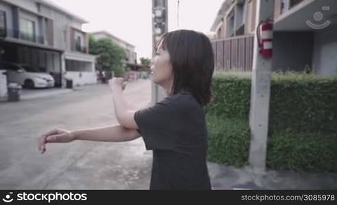 Asian woman walking home cooling down after doing exercise swinging arms, relaxing after a long day, urban houses neighborhood residential zone, positive optimistic attitude, enjoying life moments