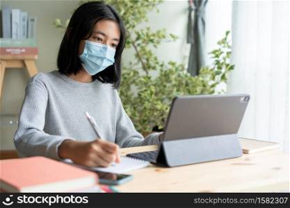 Asian woman wear medical mask while sitting learning online with laptop computer at home, concept online learning at home