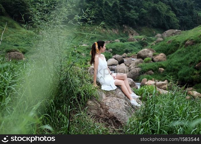 Asian woman wear white dress is sitting on the rock in forest. Freedom in the nature concept