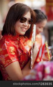 asian woman wearing chinese tradition suit and holding bamboo fan with toothy smiling face in bangkok china town