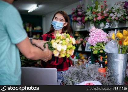 Asian Woman wearing face mask or protective mask against coronavirus crisis, Florist owner of a small florist business holding flowers for delivery to customers at her store