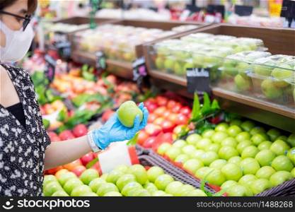 Asian woman wearing nitrile gloves and holding green apple fruit in supermarket or grocery, protect coronavirus inflection. Hygiene, new normal and life after covid-19 pandemic