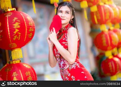 Asian woman wearing red cheongsam dress traditional decoration holding red envelopes in hand and lanterns with the Chinese text Blessings written on it Is a Fortune blessing for Chinese New Year