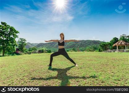 Asian woman wearing sportswear practicing yoga warrior or Virabhadrasana Pose stretching exercises muscle with yoga meditation relax and refresh health on green grass feeling happiness and comfortable