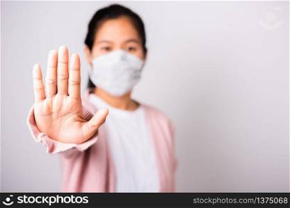 Asian woman wearing surgical protection face mask hygiene against coronavirus her raising hand stop sign, studio shot isolated on white background with copy space, COVID-19 or corona virus concept