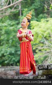 Asian woman wearing typical, traditional Thai Dress standing on an antique stone ladder. Red and gold National costume. Asian young girl wearing typical, traditional Thai Dress. Red and gold traditional dancing.