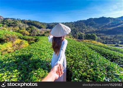 Asian woman wearing Vietnam culture traditional holding man&rsquo;s hand and leading him to green tea field.