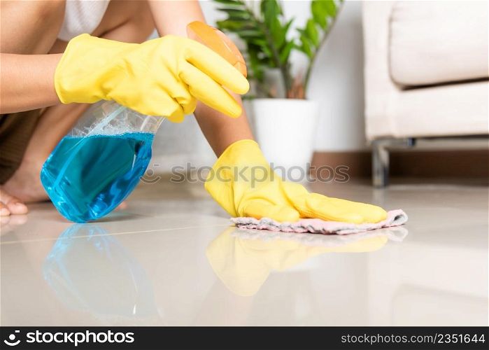 Asian woman wearing yellow rubber glover with cloth rag and detergent spray cleaning floor at home in living room, Female hands wash cleaner, housework and housekeeping concept