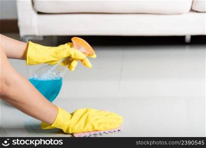 Asian woman wearing yellow rubber glover with cloth rag and detergent spray cleaning floor at home in living room, Female hands washing cleaner house worker, housework and housekeeping concept
