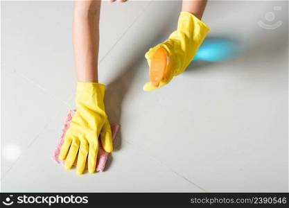 Asian woman wearing yellow rubber glover with cloth rag and detergent spray cleaning floor at home in living room, Female hands wash cleaner, housework and housekeeping concept