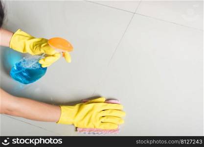 Asian woman wearing yellow rubber glover with cloth rag and detergent spray cleaning floor at home in living room, Female hands washing cleaner house worker, housework and housekeeping concept