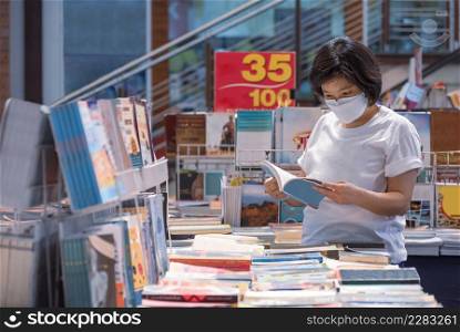 Asian woman wears protective face mask is choosing books at bookstore in shopping mall area