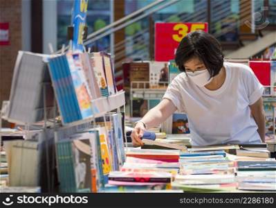 Asian woman wears protective face mask is choosing books in bookstore at shopping mall